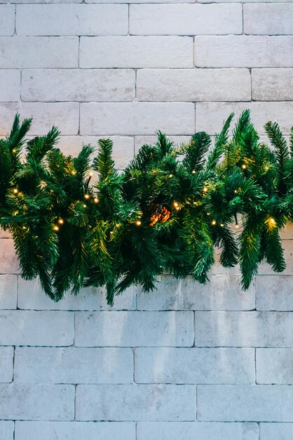 Christmas fir tree with lights on white brick background with copy space