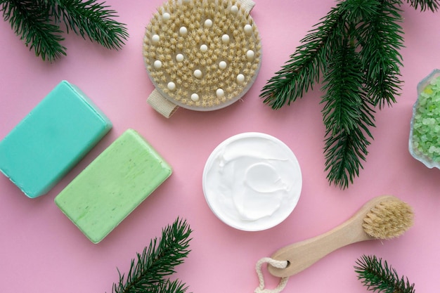 Christmas flat lay of bath products. Massage brushes, soap and body cream on pink background, top view