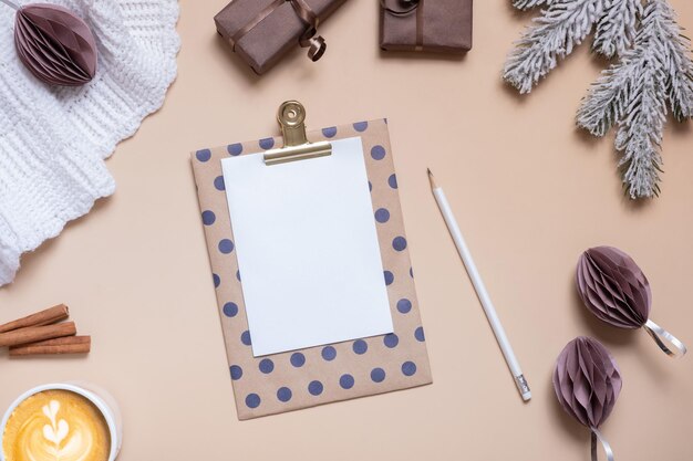 Christmas flat lay composition with a blank sheet of paper gifts and Christmas decorations on a beige background