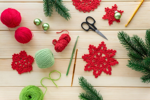 Christmas flat lay of items for needlework. Knitted snowflakes, threads and hooks on wooden background.