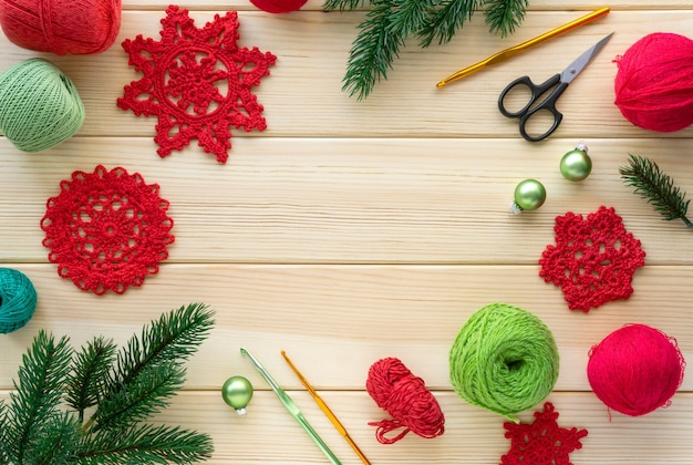 Christmas flat lay of items for needlework. Knitted snowflakes, threads and hooks on wooden background.