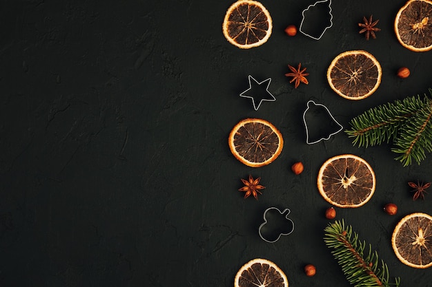 Christmas food dark background. Fir branches with cookie cutters, dry orange chips, anise and nuts. Top view. Culinary composition. Holiday card for the New Year 2022. Flat lay. Copy space