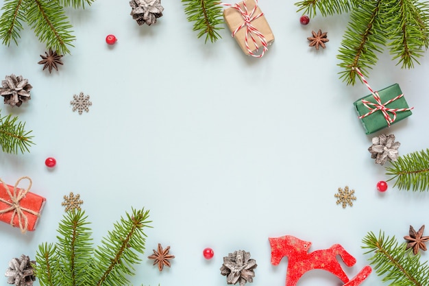 Christmas frame made of fir branches, red berries, gift boxes, retro toy and pine cones on blue background. Christmas background. Flat lay. top view with copy space