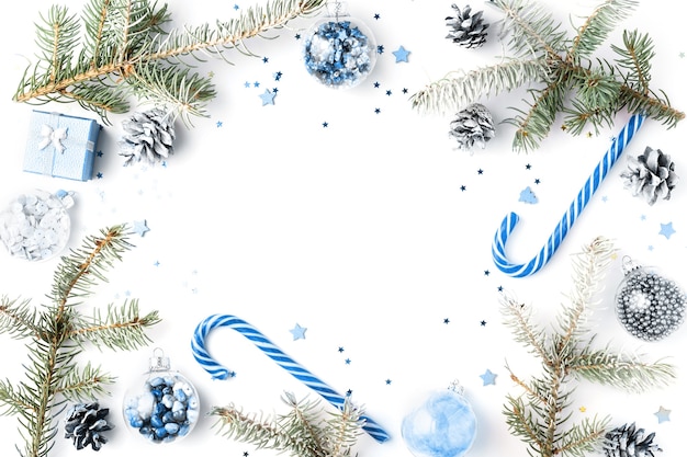 Christmas frame made of snow fir branches, blue candy canes, decorations. Christmas background, wallpaper. Flat lay, top view, copy space