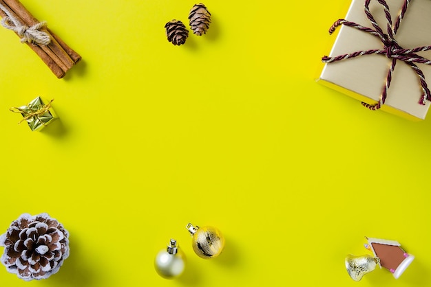 Christmas frame with gift box,cones,cinnamon and Christmas ornaments on yellow paper background