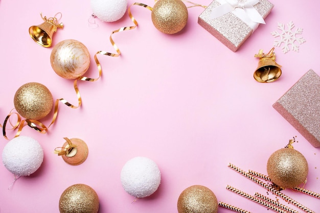 Christmas frame with gold balls gifts and bells on a pink background Flat lay style