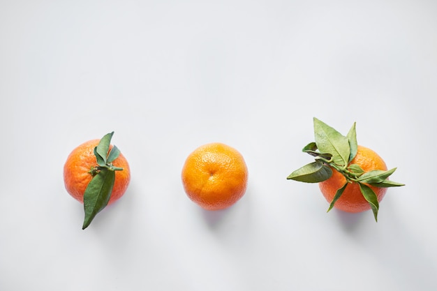 Photo christmas fruits. three orange fresh tangerines or mandarines with green leaves lie on a white background. top view.