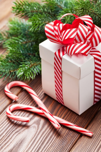 Christmas gift box, candy cane and fir tree branch on wooden table