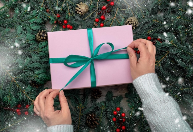 Christmas gift box in female hands Woman hands hold christmas or new year decorated gift box Christmas and New Year concept Womans hands open gift or present box decorated fir branches on table