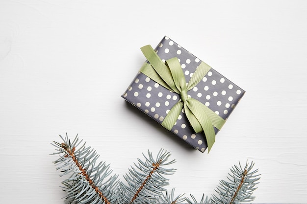 Christmas gift box and green fir tree branch on white wooden background top view flat lay Winter holiday dotted giftbox