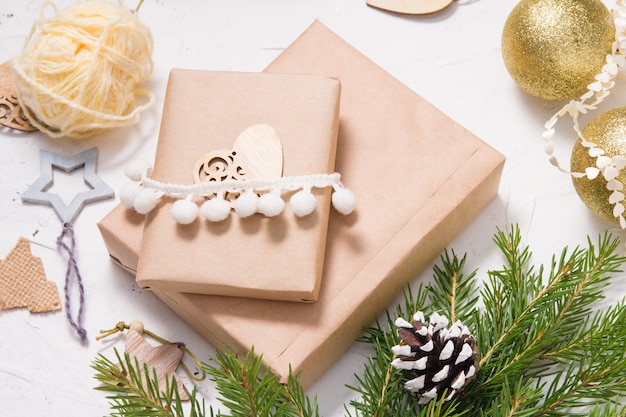 Christmas gift box packed in kraft paper and decorated with a wooden heart and fir branches, natural materials for decorating gifts on a white background, eco friendly christmas concept