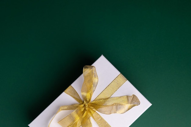 Christmas gift box present with golden ribbon on green background. Copy space for text, card, banner