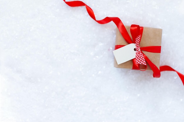 Christmas gift box with red ribbon and empty tag for text on the snow