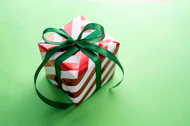 Christmas gift box with ribbon and bow on green background