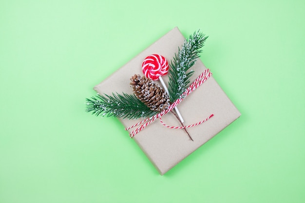 Christmas gift box wrapped in brown craft paper with corn, fir-tree and candy on green background.Christmas concept. Eco package. Focus on corn