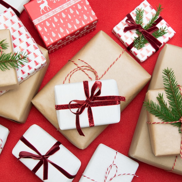 Christmas gift box wrapped in ornament paper and decorative red rope ribbon on red surface.