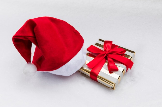 Christmas gift in a festive package and a Santa Claus hat on the snow.