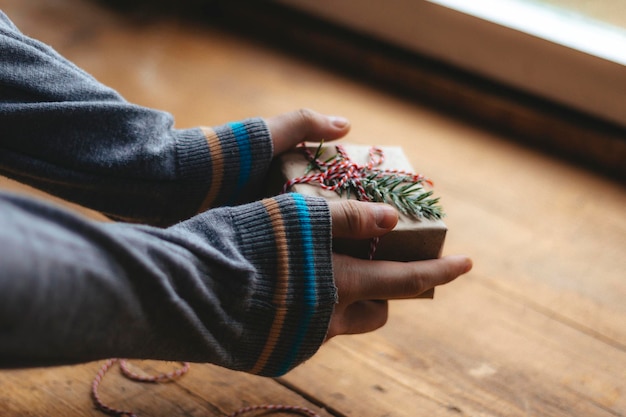 Christmas gift packaging. Men's hands in a blue sweater hold a small gift box against the background of a rustic wooden table. Selective focus