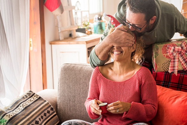 Christmas gift surprise couple with man doing a surprise to woman wife at home