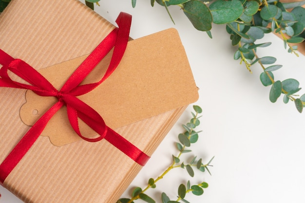 Christmas gift with red bow and greeting card on white wooden background