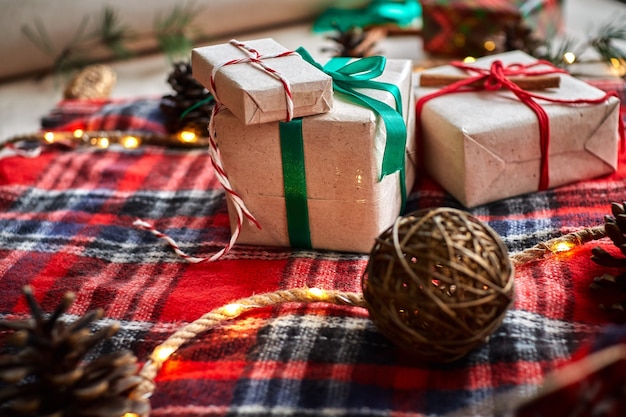 Christmas gifts on the background of a red woolen checkered plaid with garlands of cones and fir branches