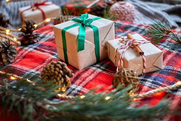 Christmas gifts on the background of a red woolen checkered plaid with garlands of cones and fir branches