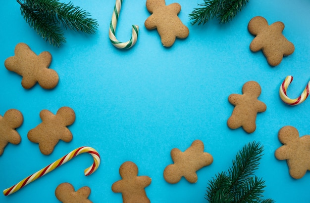 Christmas gingerbread cookies in the shape of man with lollipops and fir branches on blue background, copyspace.