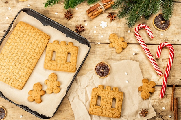 Christmas Gingerbread House and Gingerbread Men. Traditional festive New Year design, cooking process. Old wooden background, rustic style, top view