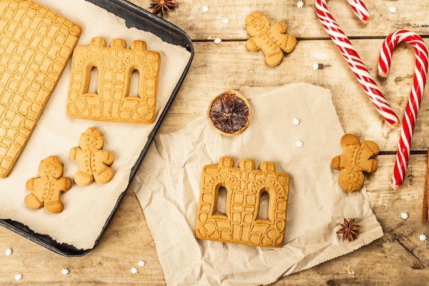 Christmas Gingerbread House and Gingerbread Men. Traditional festive New Year design, cooking process. Old wooden background, rustic style, top view