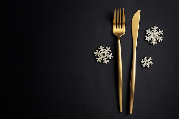 Christmas golden cutlery with snowflake on black. Flat Lay.