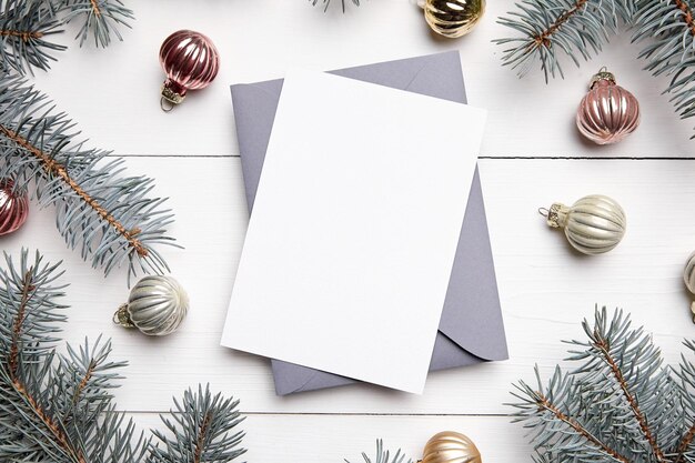 Christmas greeting card mockup with envelope green fir tree branches and balls on white wooden background top view flat lay Winter holiday card mockup with decorations