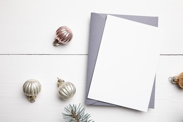 Christmas greeting card mockup with envelope green fir tree branches and balls on white wooden background top view flat lay Winter holiday card mockup with decorations