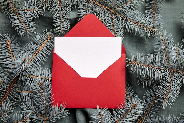 Christmas greeting card mockup with red envelope and fir tree branches on green background top view flat lay