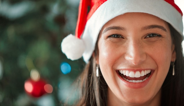 Photo christmas hat woman and face with smile in closeup for celebration of winter or december holidays at home happy female person and xmas with ornaments and decoration on tree for festive season