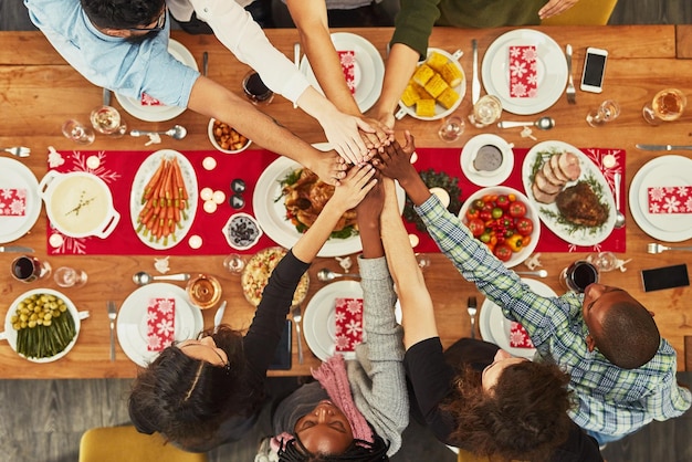 Christmas high five and food with a group of friends sitting around a dinner table together for celebration Thanksgiving hands and meal with a team enjoying a lunch on a wooden surface from above