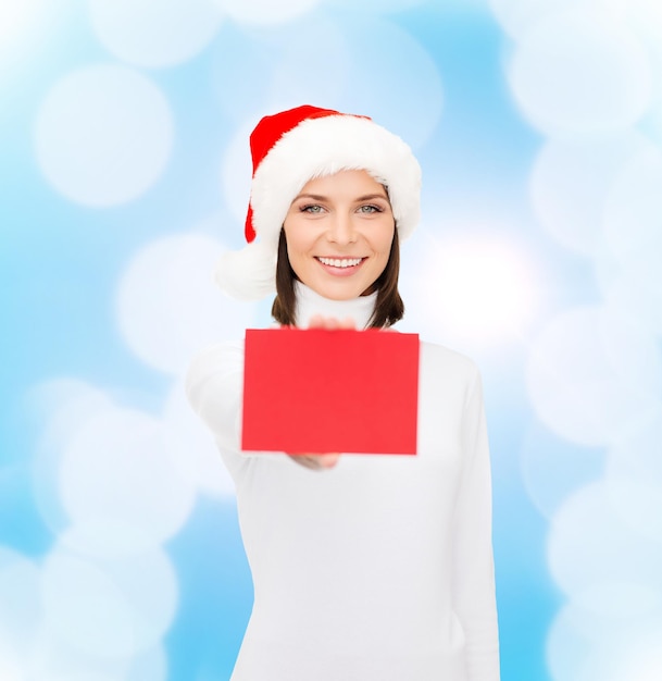 christmas, holdays, people, advertisement and sale concept - happy woman in santa helper hat with blank red card over blue lights background