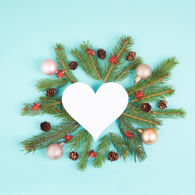 Christmas holiday background in heart shape, frame with fir branches, baubles and pine cones, winter