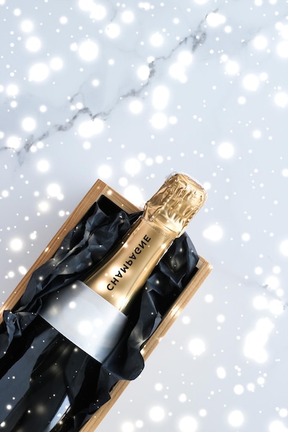 Christmas holiday champagne bottle and a gift box and shiny snow on marble background