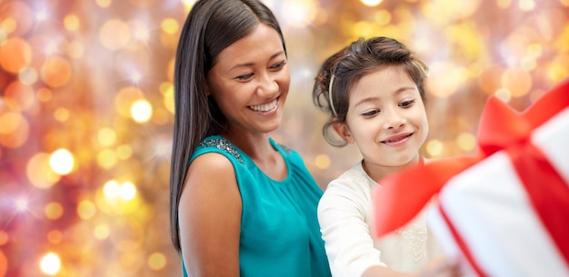 christmas, holidays, celebration, family and people concept - happy mother and child girl with gift box over lights background