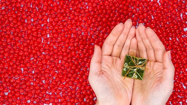 Christmas holidays concept with space for text hands holding small green gift against red color