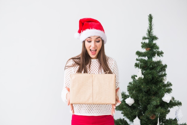 Christmas and holidays concept - young woman in santa hat holding gift box