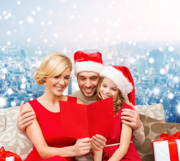 christmas, holidays, family and people concept - happy mother, father and little girl in santa helper hats with gift boxes over snowy city background