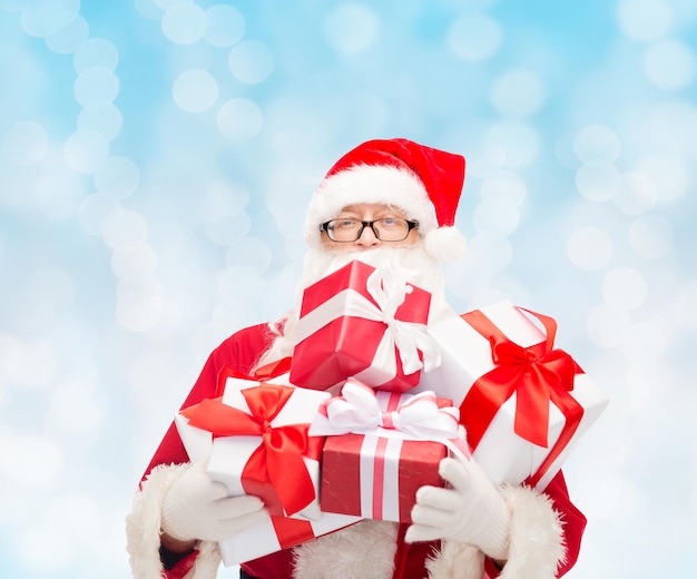 christmas, holidays and people concept - man in costume of santa claus with gift boxes over blue lights background