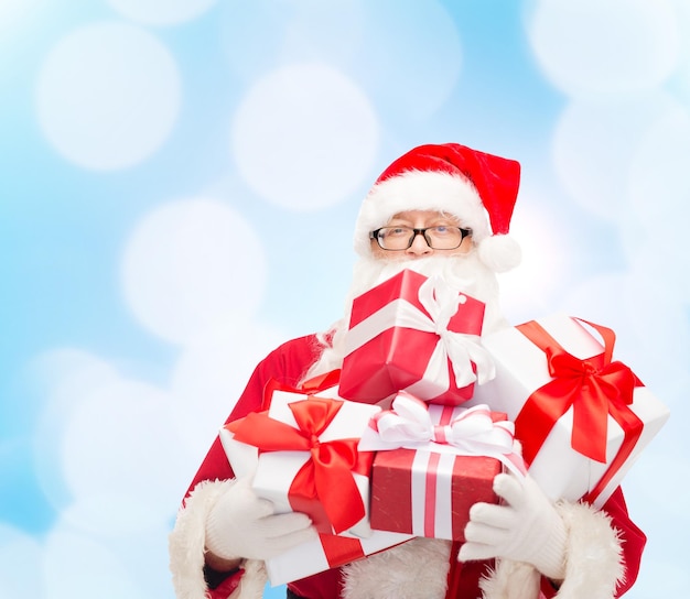 christmas, holidays and people concept - man in costume of santa claus with gift boxes over blue lights background