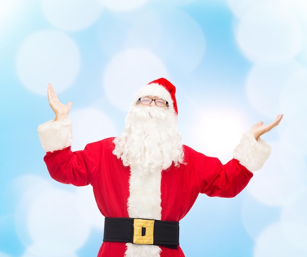 christmas, holidays and people concept - man in costume of santa claus with raised hands over blue lights background