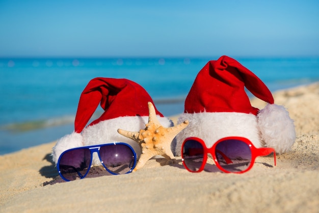 Christmas holidays and Romantic New Year at Sea. Santa hats and sunglasses on sandy beach