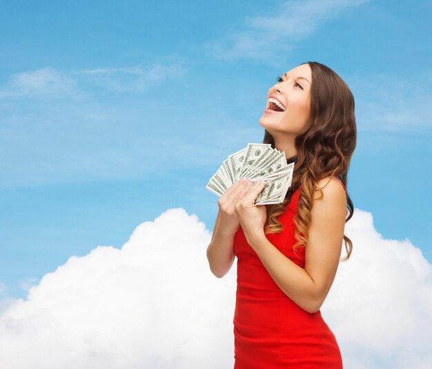 christmas, holidays, sale, banking and people concept - smiling woman in red dress with us dollar money over blue sky and cloud background