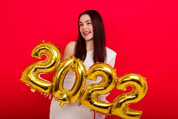 Christmas holidays - A young woman in a white dress holds the numbers 2022 on a red background