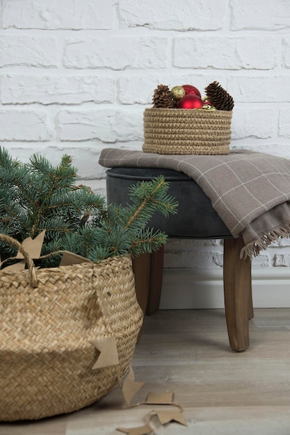 Christmas home decoration rustic straw basket with fir branches knitted basket with christmas toys on a chair on bricks background