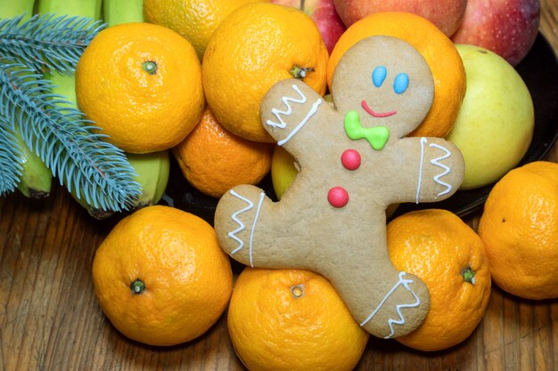 Christmas homemade gingerbread in the form of a little man on a wooden table among tropical fruits.